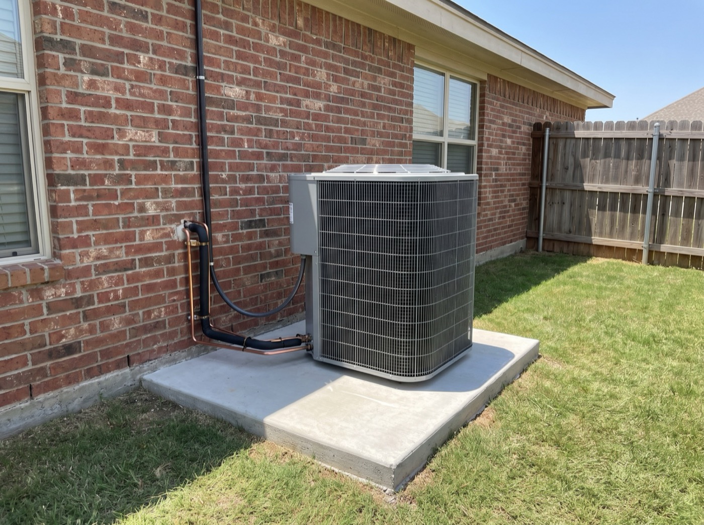 A new unbranded AC condenser sitting level on a fresh concrete pad with a clean copper lineset